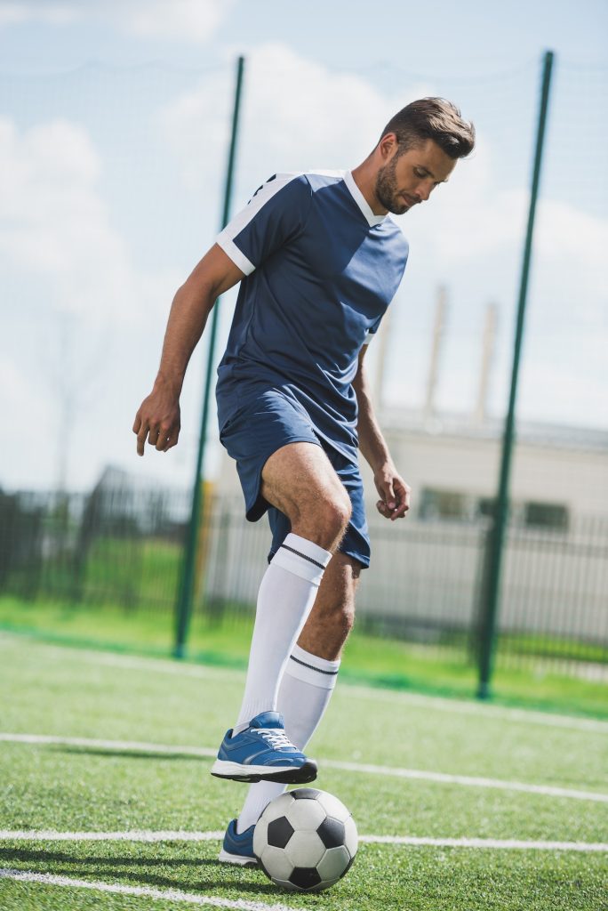 athletic soccer player training with ball on soccer pitch